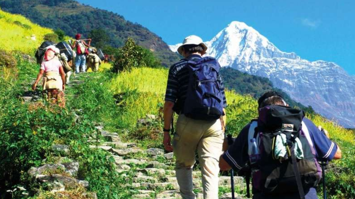 Travelers hiking through green mountain trails toward snowy peaks, symbolizing healthy tourism and mental wellness