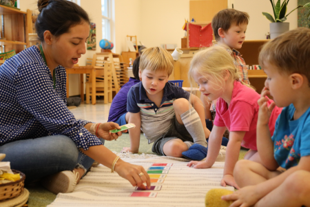 A Montessori teacher engages children in a colorful card activity, fostering learning and creativity in a vibrant classroom setting.