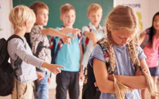 A young girl looks sad while a group of boys point and laugh at her in a classroom, illustrating one of the social problems in the education system.